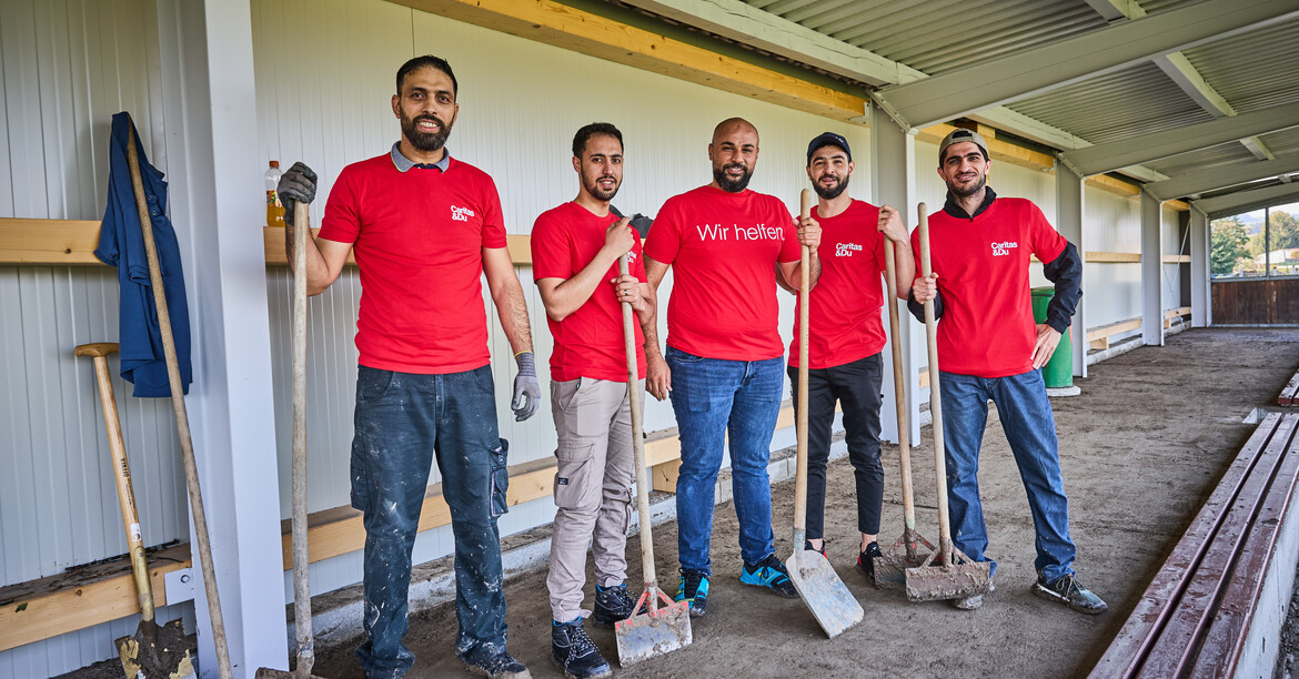 Fünf Freiwillige mit Werkzeug in roten Caritas-Shirts bei Aufräumarbeiten nach einem Hochwasser