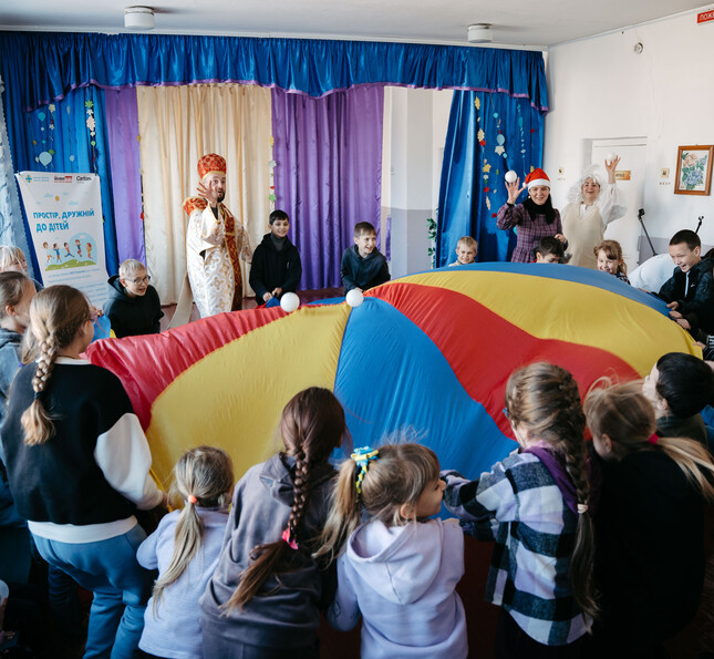 Kinder halten ein buntes Schwungtuch in einer Betreuungseinrichtung