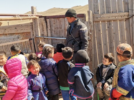 Eine Gruppe von Kindern vor einem Zaun, ein Erwachsener steht dabei
